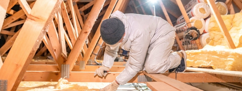 Arbeiter installiert Dämmwolle auf Dachboden für verbesserte Energieeffizienz