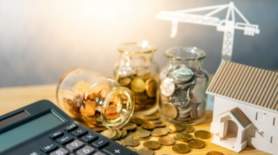 Symbolisches Geld neben einem Taschenrechner und modernen, energieeffizienten Gebäude
