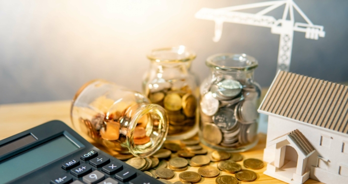 Symbolisches Geld neben einem Taschenrechner und modernen, energieeffizienten Gebäude
