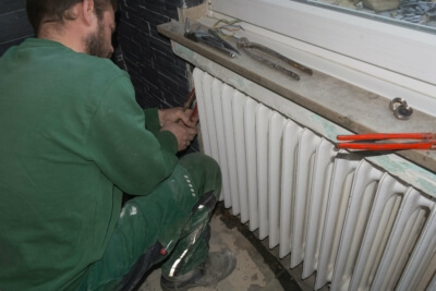 Handwerker entfernt alten Heizkörper für moderne Heizung im Rahmen der Energiewende Handwerker bei der Entfernung eines alten Heizkörpers, symbolisch für den Anstieg der Sanierungsbereitschaft in Deutschland