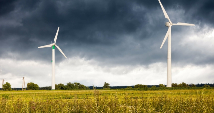 Windturbinen in ländlicher Landschaft unter stürmischem Himmel – Notwendigkeit des Ausbaus erneuerbarer Energiequellen laut Prognos AG