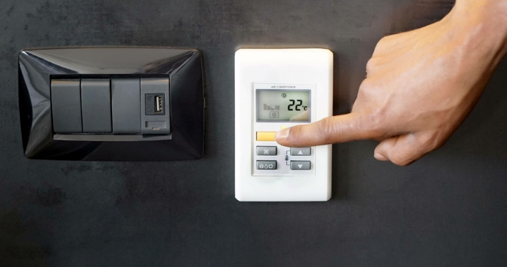 Hand justiert Heizungssteuerung auf 22 Grad, symbolisiert energieeffiziente Maßnahmen und KfW-Fördermöglichkeiten