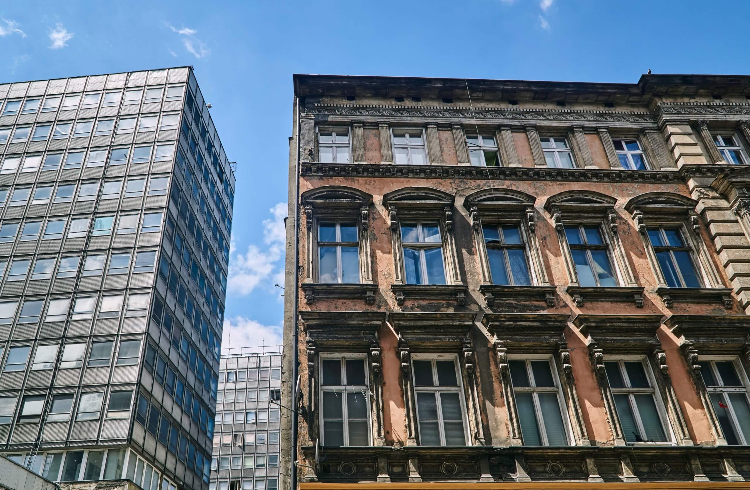 Historisches und modernes Gebäude in der Stadt, beide betroffen von der EU-Sanierungspflicht zur Erreichung der Klimaneutralität bis 2030.