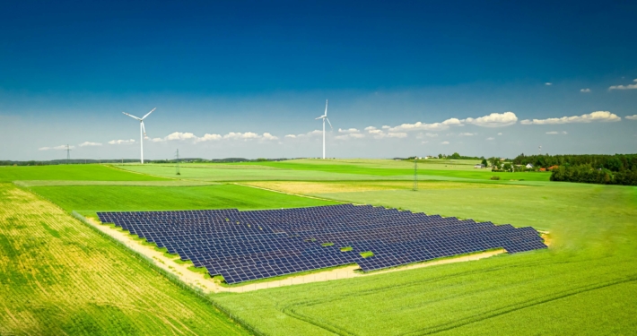 Weitläufige Photovoltaikanlage auf einem Feld mit Windkraftanlagen im Hintergrund, symbolisiert den Ausbau erneuerbarer Energien gemäß EEG 2025
