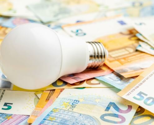 Eine Glühbirne liegt auf Euro-Geldscheinen als Symbol für Energiekosten und Fördergelder für Sanierungen und Heizungen