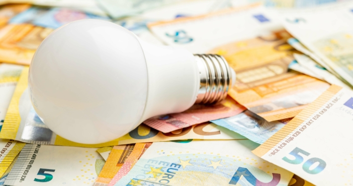 Eine Glühbirne liegt auf Euro-Geldscheinen als Symbol für Energiekosten und Fördergelder für Sanierungen und Heizungen