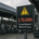Warnschild mit der Anzeige 2,76 GWh und dem Hinweis „Schwellenwert überschritten“ vor einer Industriehalle mit Maschinen und Solaranlage