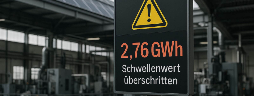 Warnschild mit der Anzeige 2,76 GWh und dem Hinweis „Schwellenwert überschritten“ vor einer Industriehalle mit Maschinen und Solaranlage