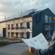 Energieberater mit Bauplan vor einem sanierten Gewerbegebäude mit Photovoltaikanlage und Wärmepumpe
