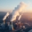 Kühltürme einer Industrieanlage mit aufsteigendem Dampf bei Sonnenuntergang, Symbol für energieintensive Produktion und CO₂-Debatte