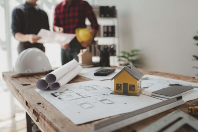 Energetische Sanierung jetzt planen – Fördermittel-Kürzung 2025 beachten Zwei Planer besprechen energetische Sanierung eines Hauses mit Bauplänen und Modell auf dem Tisch