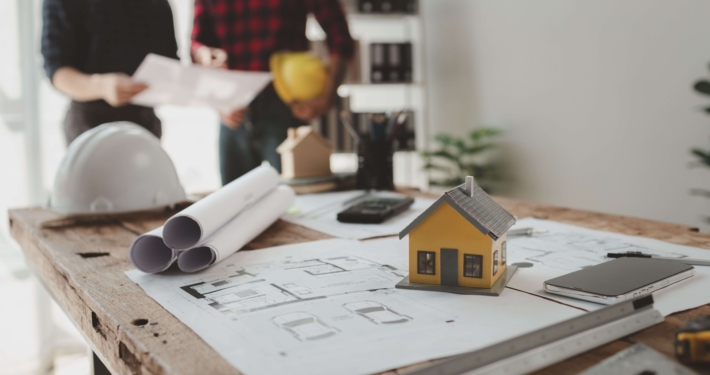 Zwei Planer besprechen energetische Sanierung eines Hauses mit Bauplänen und Modell auf dem Tisch