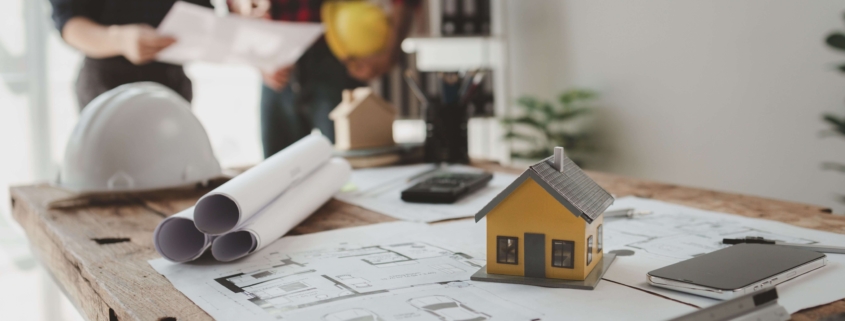 Zwei Planer besprechen energetische Sanierung eines Hauses mit Bauplänen und Modell auf dem Tisch