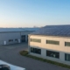 Industriehallen mit großflächigen Photovoltaikanlagen auf den Dächern und einer Wärmepumpen-Außeneinheit im Vordergrund bei Sonnenaufgang.