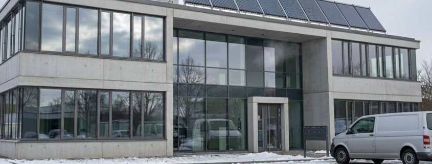 Modernes Gewerbegebäude mit Solarkollektoren und Wärmepumpe auf dem Dach im Winter – Beispiel für Heizungsmodernisierung gemäß 65-Prozent-Regel