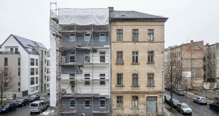 Teilmodernisiertes Mehrfamilienhaus mit Gerüst neben unsaniertem Altbau – Symbolbild für sinkende Sanierungsquote in Deutschland
