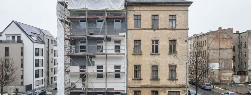 Teilmodernisiertes Mehrfamilienhaus mit Gerüst neben unsaniertem Altbau – Symbolbild für sinkende Sanierungsquote in Deutschland