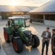 Energieberater bespricht mit Landwirt die effiziente Nutzung von Photovoltaik und das Laden eines Elektro-Traktors auf einem modernen Hof.