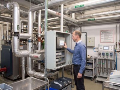 Techniker prüft Bedienpanel eines Lüftungsschaltschranks in der Technikzentrale eines Krankenhauses