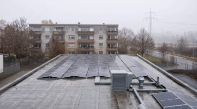 Flachdach einer Produktionshalle mit Photovoltaik, dahinter ein Wohnhaus und eine Freileitung an einem nebligen Novembermorgen