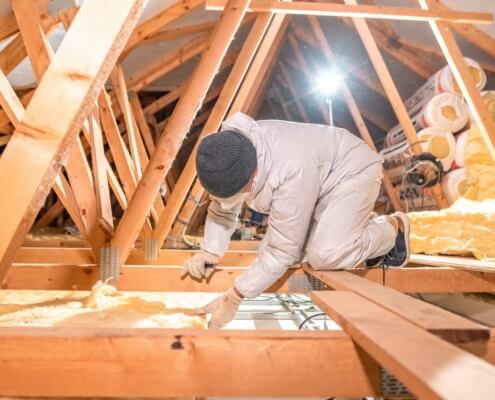 Arbeiter installiert Dämmwolle auf Dachboden für verbesserte Energieeffizienz