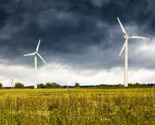 Windturbinen in ländlicher Landschaft unter stürmischem Himmel – Notwendigkeit des Ausbaus erneuerbarer Energiequellen laut Prognos AG